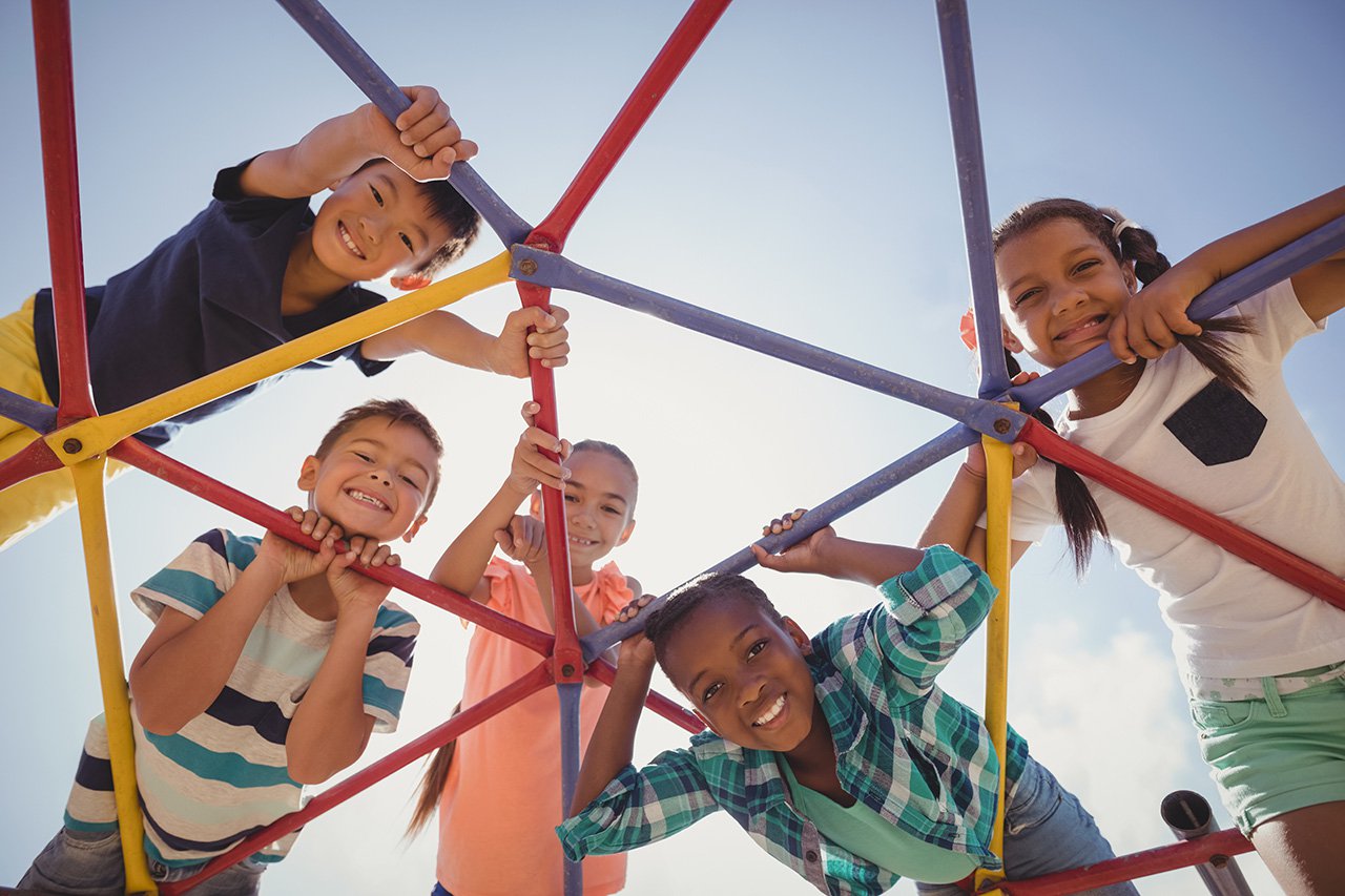 Portrait-of-happy-schoolkids-looking-through-dome-climber-